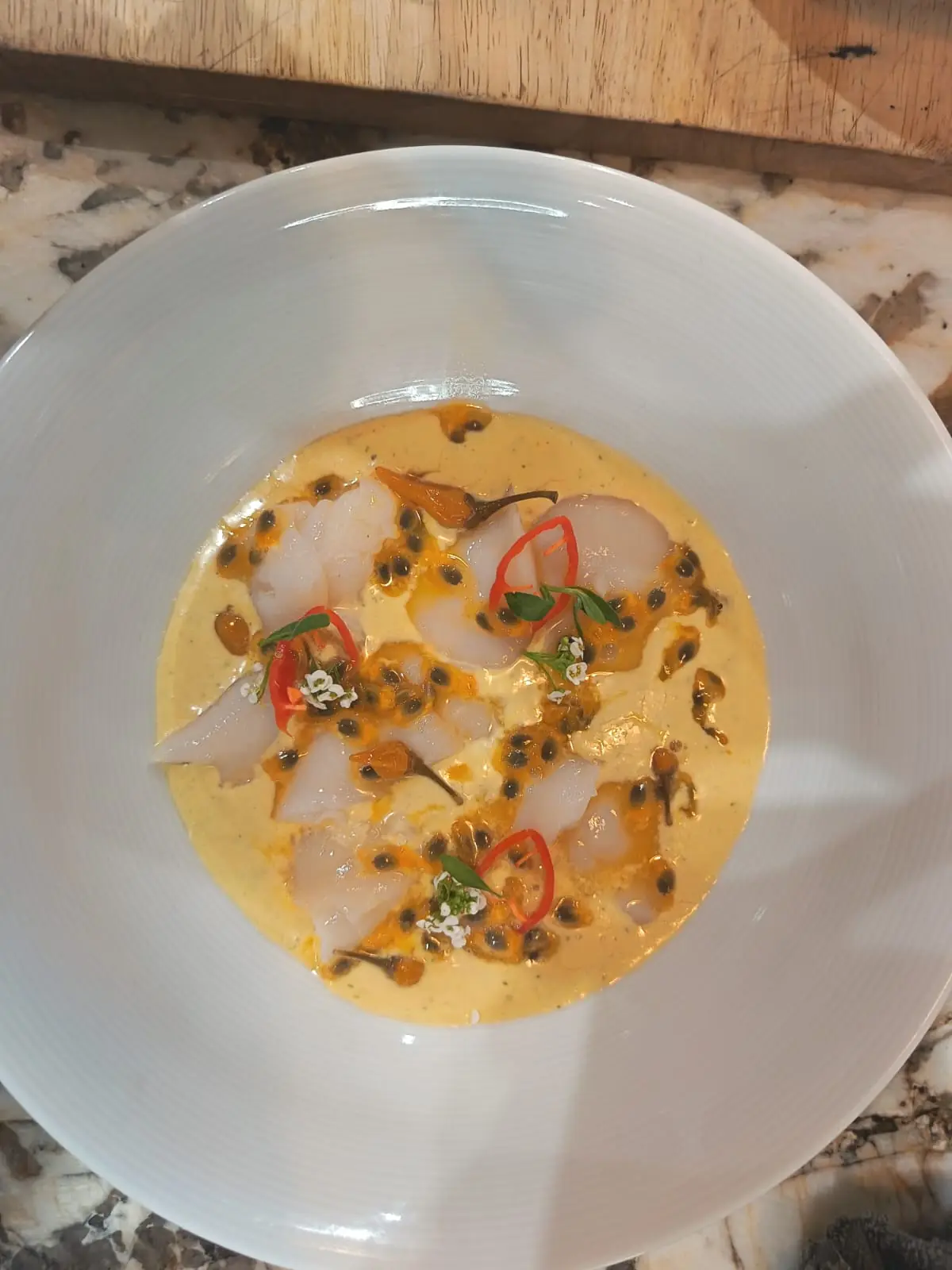 Poisson cru en fines tranches, sauce jaune, graines de fruit de la passion et piment, dans une grande assiette blanche